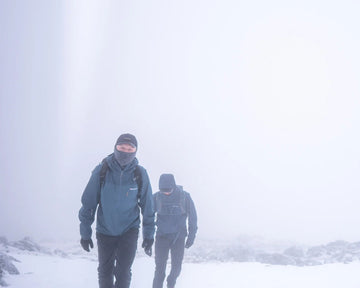 Two people walking in a snowy landscape with a foggy background