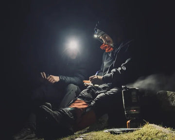 Two people sitting on a rock at night with flashlights